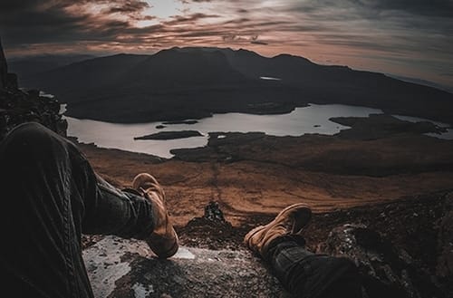 man sitting on the top of the Mountain and looking at the view in Scotland